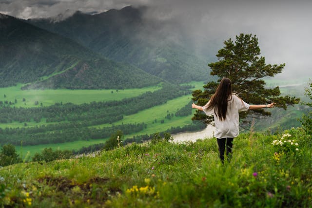 a woman standing on a hill with her arms outstretched