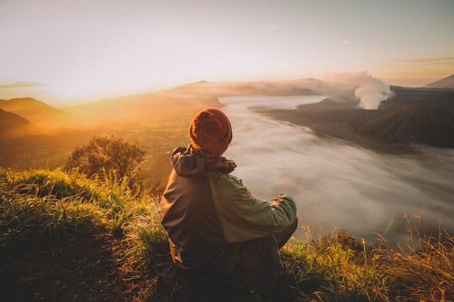 a person sitting on a hill looking at the sunset
