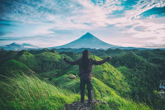 a person standing on a rock with arms outstretched in front of a mountain