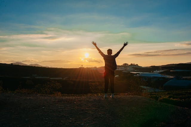 a man standing on a hill with his arms raised
