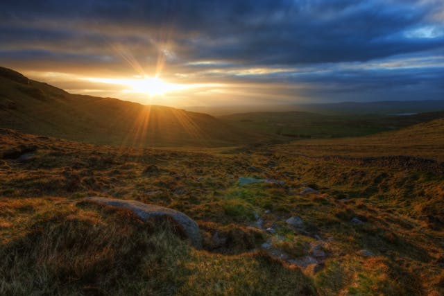 a sun shining through the clouds over a grassy field