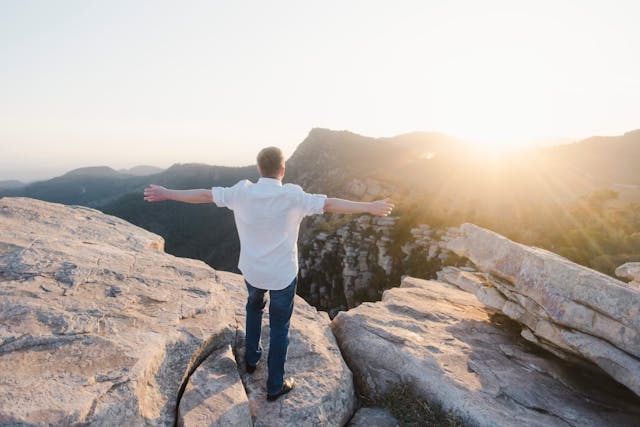 A man standing on a rock, stretching his arms at sunset.