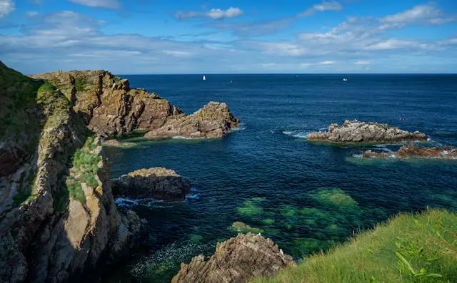 a rocky coastline with a body of water and a sailboat in the distance