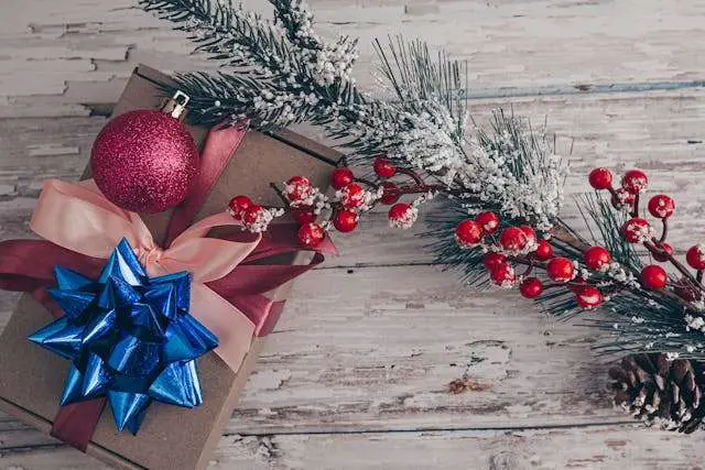 A Christmas gift box with a bauble and a fir tree branch on a wooden table.