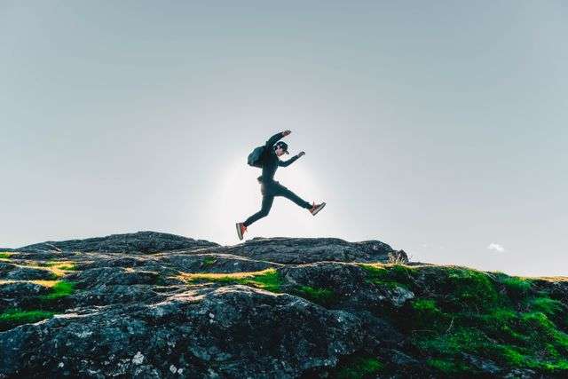 A person jumping over rocks with a clear sky background.