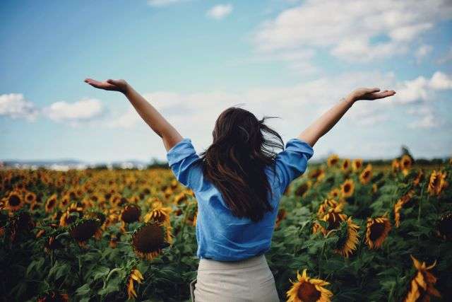 Woman in sunflower field, arms raised.